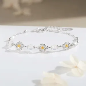 Elegant silver daisy charm bracelet with white translucent beads on a white reflective surface