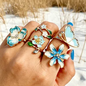 Una toma detallada de anillos de flores y mariposas de esmalte azul vibrante en una mano
