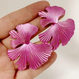 Gros plan de boucles d'oreilles feuilles en métal rose vif tenues en main pour l'échelle