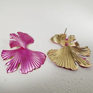 Détail de boucles d'oreilles en forme de feuille d'éventail rose et doré métallique.