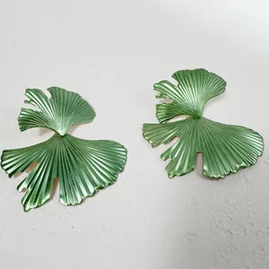 Vue macro détaillée de grandes boucles d'oreilles feuilles de ginkgo vertes au fini métallique.