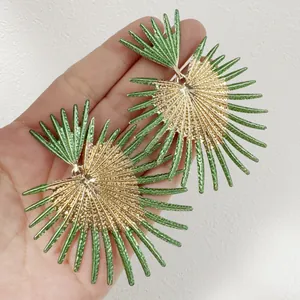 Gros plan de boucles d'oreilles rétro surdimensionnées en forme d'éventail or et vert.