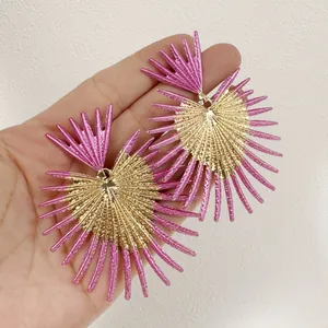 Gros plan de boucles d'oreilles feuilles dorées à pointes roses tenues pour l'échelle.