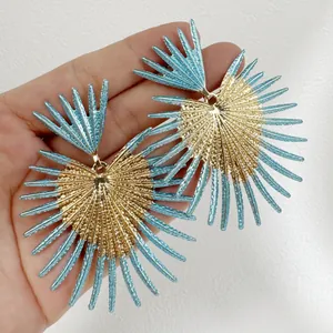 Gros plan de boucles d'oreilles rétro dorées et bleues en forme d'éventail en main