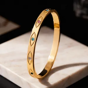 Close-up of golden stainless steel bangle featuring multicolored stone-set eye motifs.