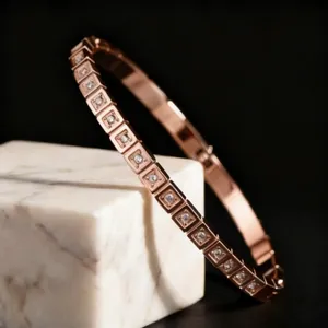 Primer plano de un brazalete de acero inoxidable oro rosa con engastes cuadrados de cristal.