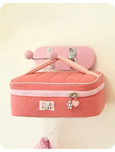 Close-up of a coral pink quilted makeup bag with a cute logo patch and decorative charms.