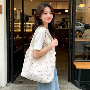 Close-up of a large capacity white polka dot canvas tote bag worn by a model in a cafe