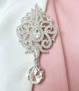 Elegant vintage silver-toned brooch with clear crystal teardrop pendant on pink fabric