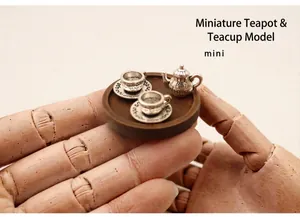 Macro view of a miniature metal tea set held on a fingertip for dollhouse decor