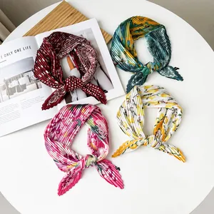 Detailed view of four pleated satin silk scarves with vibrant floral and lemon prints.