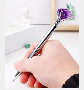 Close-up of a hand holding a silver metal ballpoint pen with raw purple amethyst
