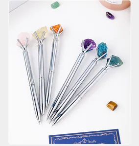Detail of silver metal ballpoint pens topped with colorful natural raw crystal stones.