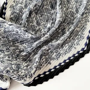 Close-up of pleated silk scarf featuring intricate blue paisley and striped border.