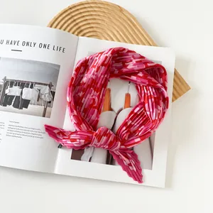 Detailed macro view of a pink and red pleated satin silk scarf on a magazine backdrop