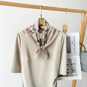 Elegant pleated silk square scarf with vintage chain print on a beige dress detail