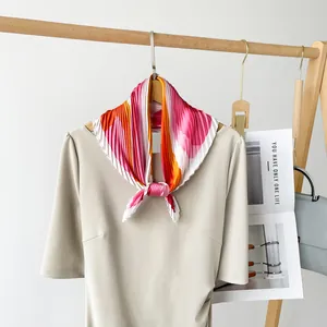 Floral printed pleated silk scarf tied around a beige dress neck on a wooden rack