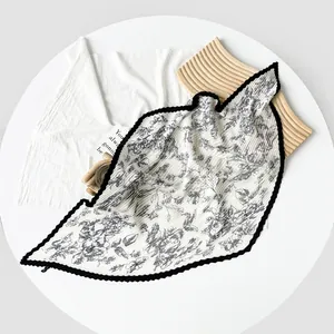 Elegant white pleated silk scarf with black floral print and wavy scalloped edge.