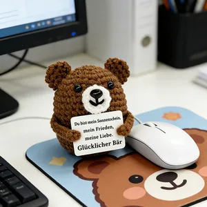 Close-up of a handmade crocheted brown bear holding a sentimental German card on a desk