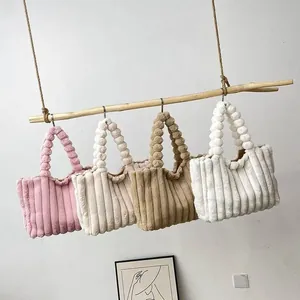 Detailed view of plush corduroy tote bags in four soft colors hanging on display