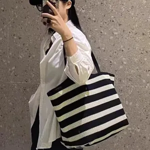 Stylish black and white striped woven tote bag shown on model in a lifestyle setting