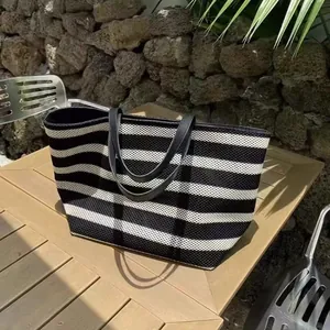 Wide view of a black and white striped woven tote bag on a wooden outdoor table.