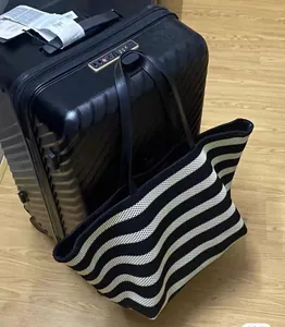 Black and white striped knitted tote bag shown with a suitcase for travel context.