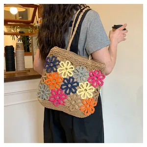 Lifestyle detail of a handmade woven straw tote bag with colorful flower patterns.