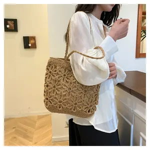 Close-up view of a hand-woven beige tote bag with intricate hollow flower patterns.
