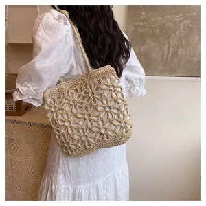 A back view of a model carrying a floral hollow-out woven straw tote bag in white dress.