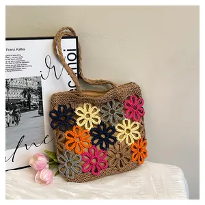 Handmade crochet tote bag with colorful floral patterns on a white table.