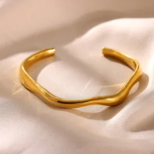 Detail of a minimalist irregular wavy cuff bracelet in gold-plated stainless steel.
