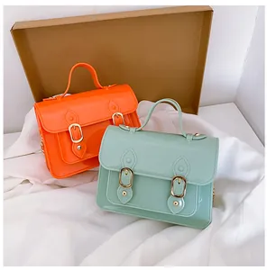 Detailed view of glossy orange and mint green jelly Cambridge satchel bags on white fabric