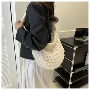 Detail view of a large cream bubble puff shoulder bag worn with a stylish outfit.