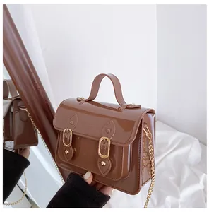 Side view of a brown jelly Cambridge bag with decorative buckles and a gold chain strap.
