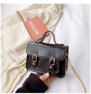 High-gloss black jelly satchel bag featuring golden buckles and a fine chain strap.
