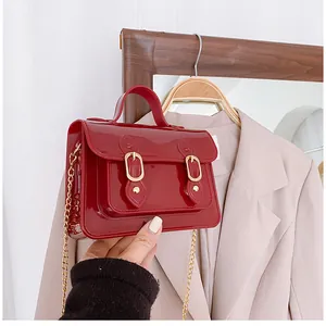 Close-up of a stylish red glossy jelly Cambridge mini satchel bag with a gold chain strap