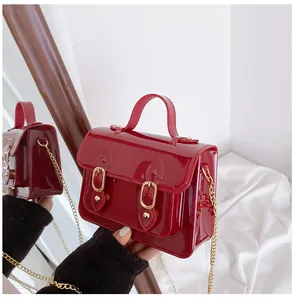 Close-up of a glossy red jelly satchel bag with gold chain strap and twin buckles