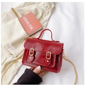 Detail of a red jelly Cambridge bag with a glossy finish and gold chain strap.