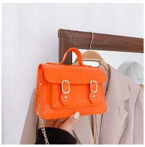 Close-up of a vibrant orange jelly Cambridge bag with a gold chain strap held by hand