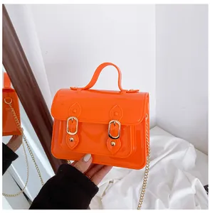 Detailed view of a bright orange jelly Cambridge bag held by hand with gold chain