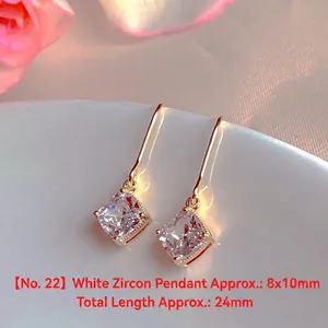 Close-up of elegant gold-tone drop earrings featuring square white zircon stones