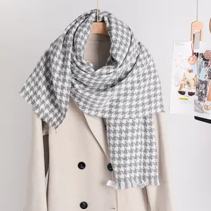 Detail shot of a thick grey and white houndstooth scarf draped over a stylish beige winter coat