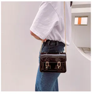 Model wearing a glossy black jelly Cambridge satchel bag with elegant gold chain strap