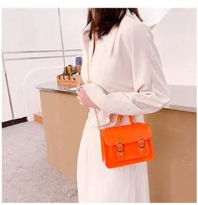 Detail view of a bright orange jelly Cambridge satchel with a gold chain strap