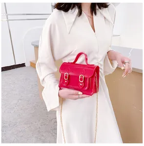 Detailed shot of a red jelly mini satchel with gold chain strap held by a model