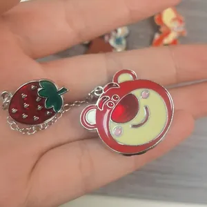 Close-up of a Lotso bear and strawberry enamel pin with silver chain