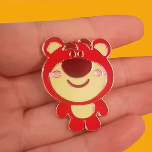 Close-up of a pink cartoon bear enamel pin held in hand with a yellow background