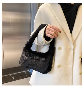 Close-up of a stylish black plush underarm bag held by a model in a white coat.