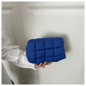 Detailed view of a vibrant blue puffer quilted cosmetic bag held by hand in a minimalist setting
